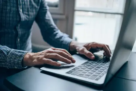 man in button down shirt typing on laptop